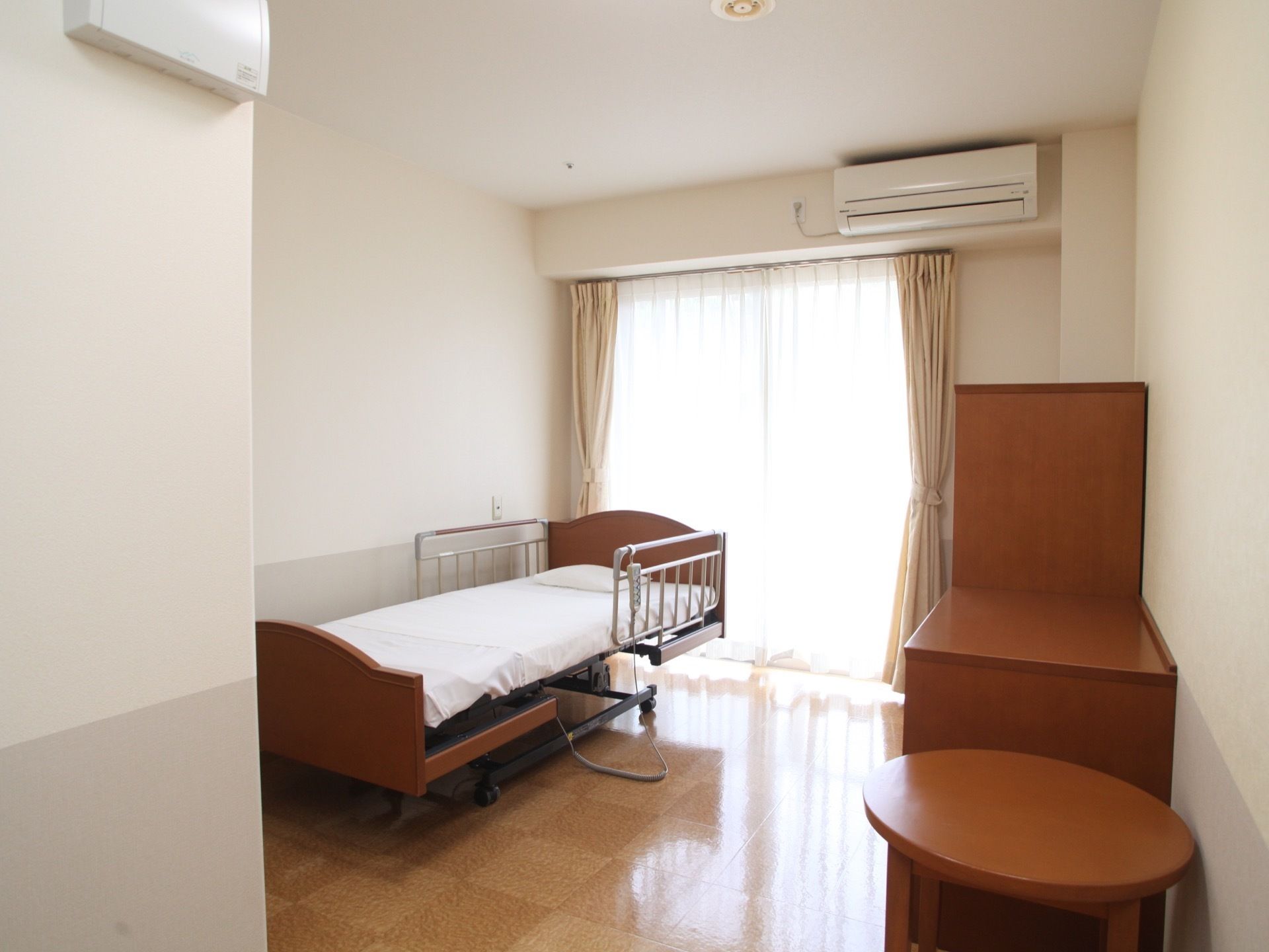 居室には、エアコンが備わっており、丸テーブルや収納家具、電動で介護を補助する機能が付いたベッドが設置してある。
