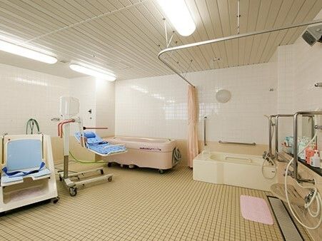 カーテン付きの一人用の浴槽が設置された浴室にはピンクの機械浴もあり、ストレッチャータイプのリフトも置かれている。