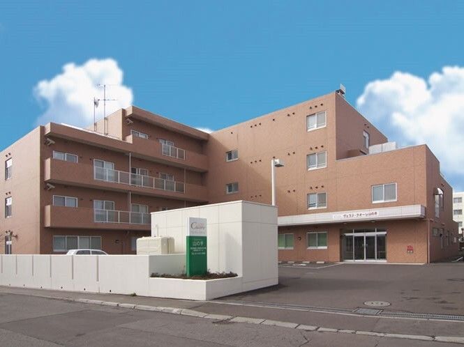 ブラウン系の寝具がセットされた4階建てで、広い駐車場があり、玄関の屋根部分にはホーム名が書かれている。