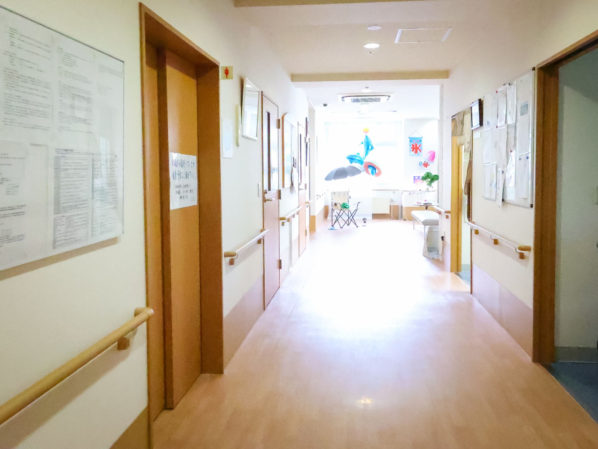 両側の扉が付いた白い壁に手すりが設けられた直線の廊下