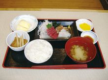 黒いトレーの上に並べられた定食風の食事。メインの刺身と汁物、白いご飯に小鉢が複数。