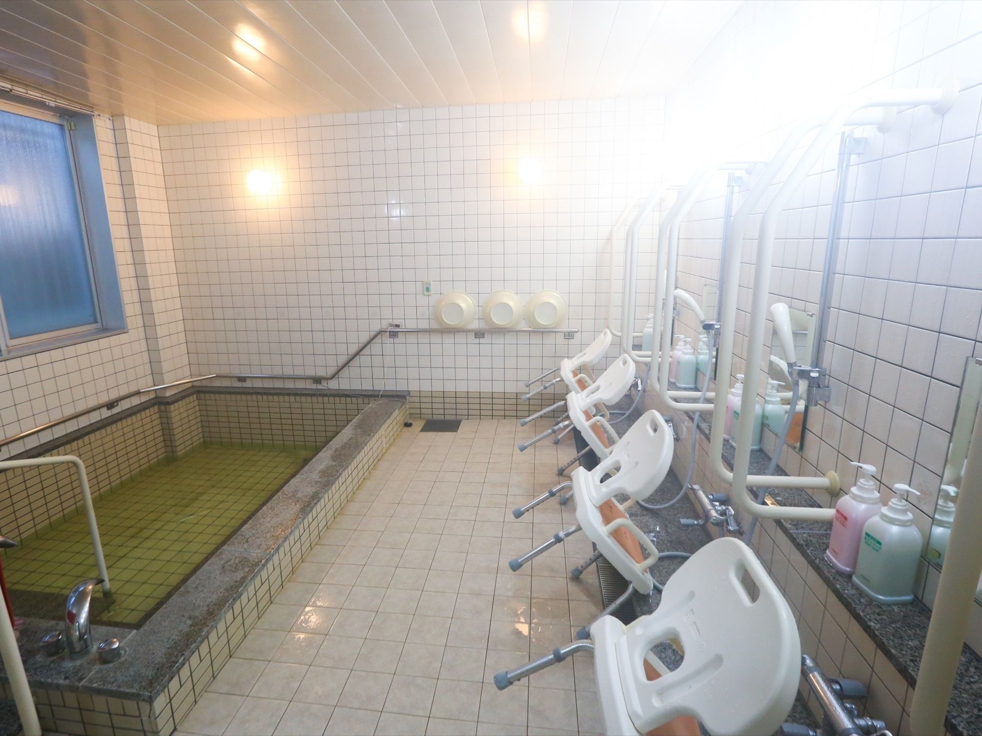 大浴場の壁には手すりがあり、丸い照明が２個取り付けられている。また洗い場にはシャワーチェアが４脚置かれている。