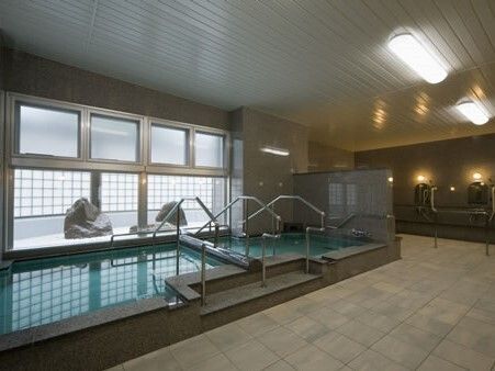 窓から枯山水庭園を眺めることができる旅館の浴室のような雰囲気の大浴場。大きな浴槽には手すりも付いている。