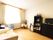 レースカーテンとカーテンが付いた大きな窓があるフローリングの部屋には寝具付きベッドやタンスがある。