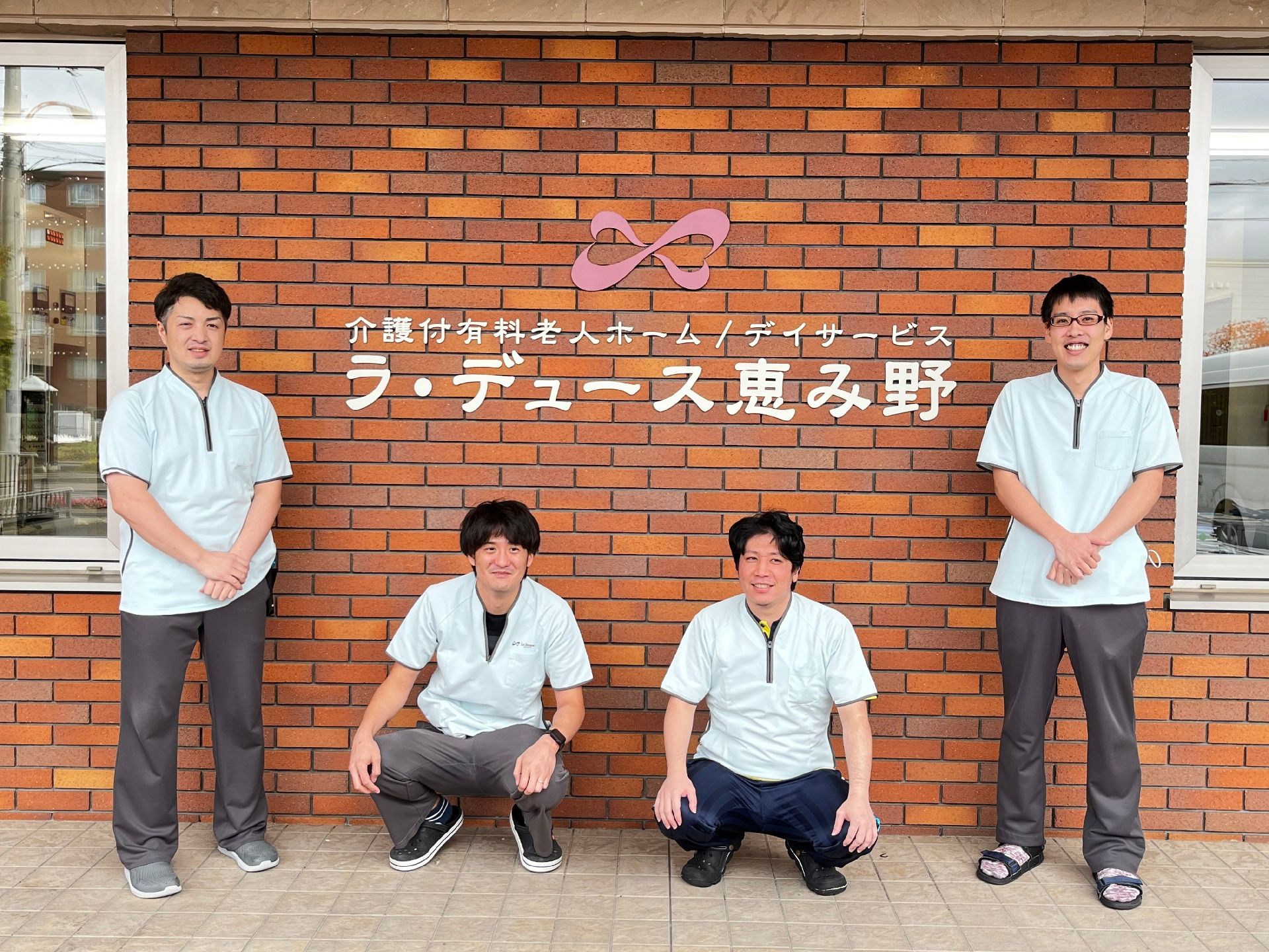 ラ・デュース恵み野の看板の前でポーズをとる施設のスタッフの様子