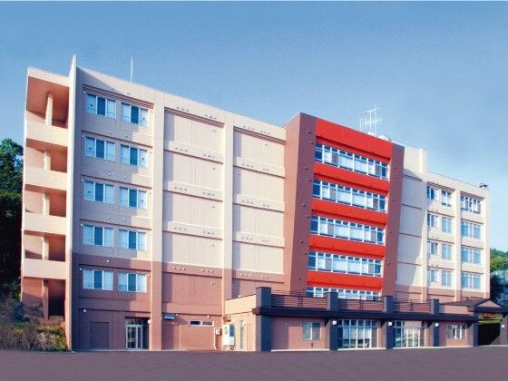日当たりのいい場所に建っている6階建ての建物はベージュとブラウンで中央部分が赤い外壁。