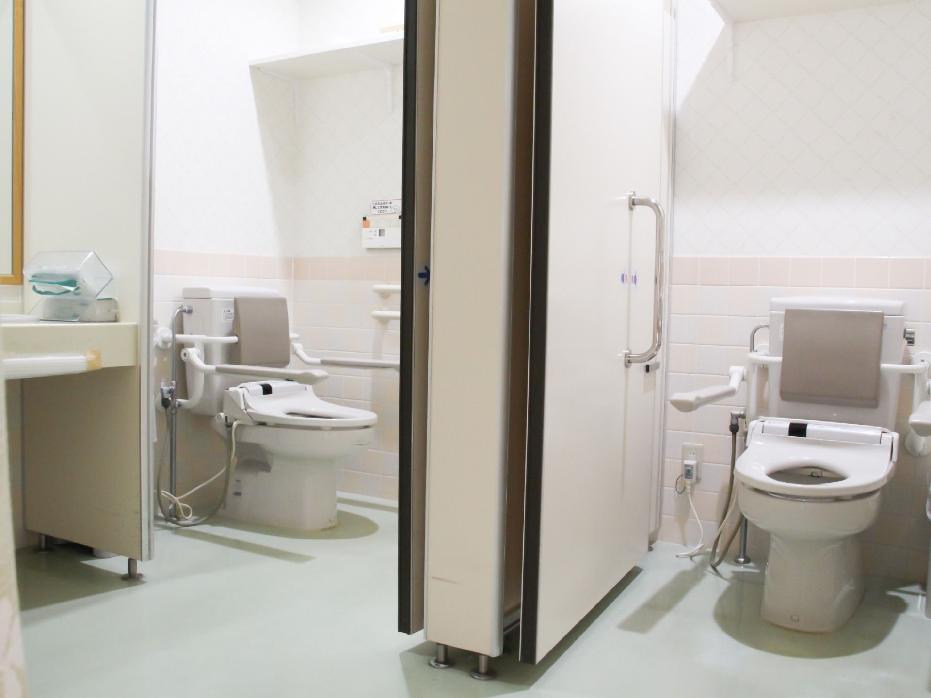 ２ヵ所に区切られた個室のそれぞれにタンク付きの洋式トイレがある。便座の背面には灰色の背もたれが設置されている。