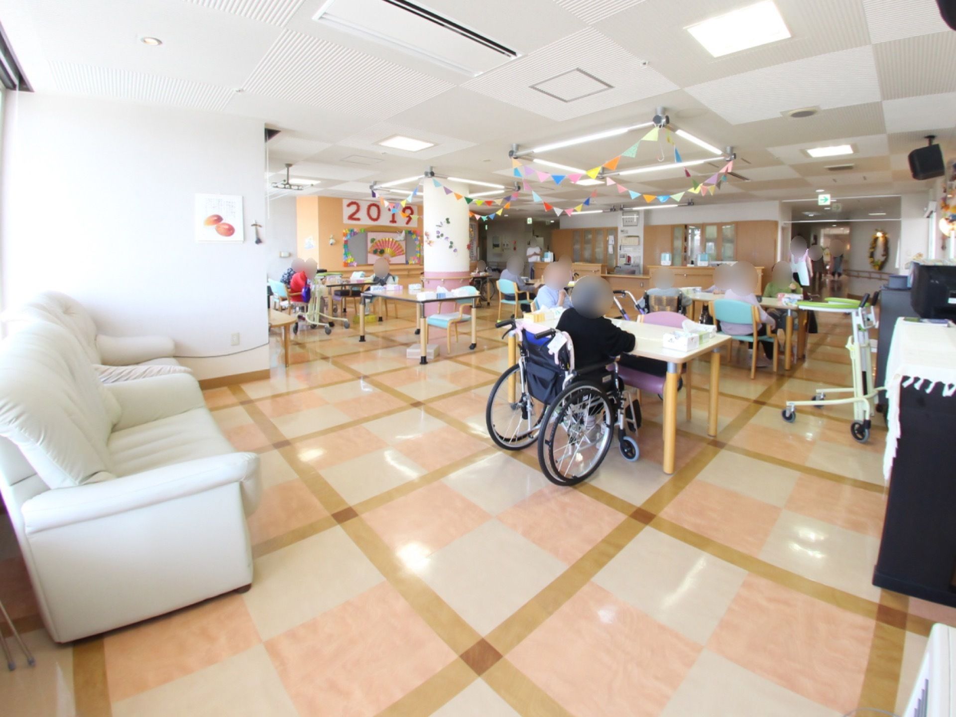 薄いオレンジ色とベージュ色と茶色いタイルの床の部屋がある。白いソファーが置いてあり、天井に手作りの飾り付けがされている。