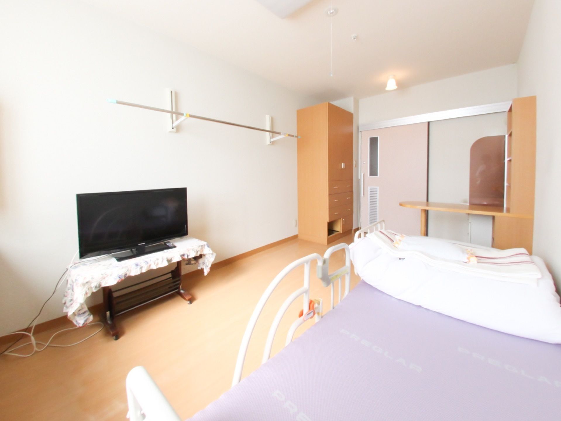 木目のフローリングの床の洋室がある。部屋の出入口はスライドドアが設置され、壁際に薄型テレビが置いてある。
