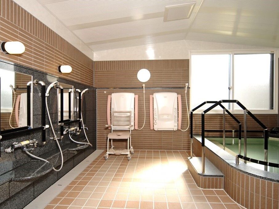 鏡付きのシャワーが左側にずらりと並んでいて、右側には大きな浴槽があり、手すりが設置されている。
