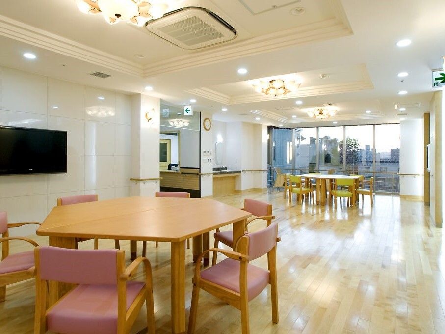 六角形のダイニングテーブルが複数置かれ、大きな壁掛けテレビが設置されたフローリングの共有スペース。