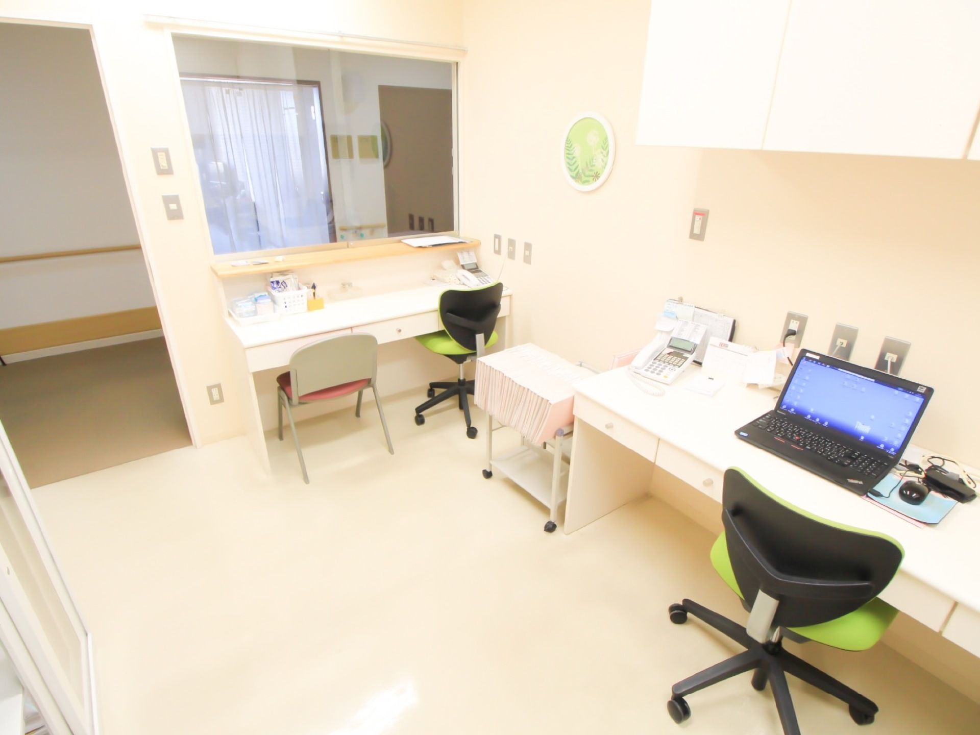 清掃が行き届いた、白を基調とした部屋にデスクと椅子が置かれており、机の上にはノートパソコンと電話が設置されている。
