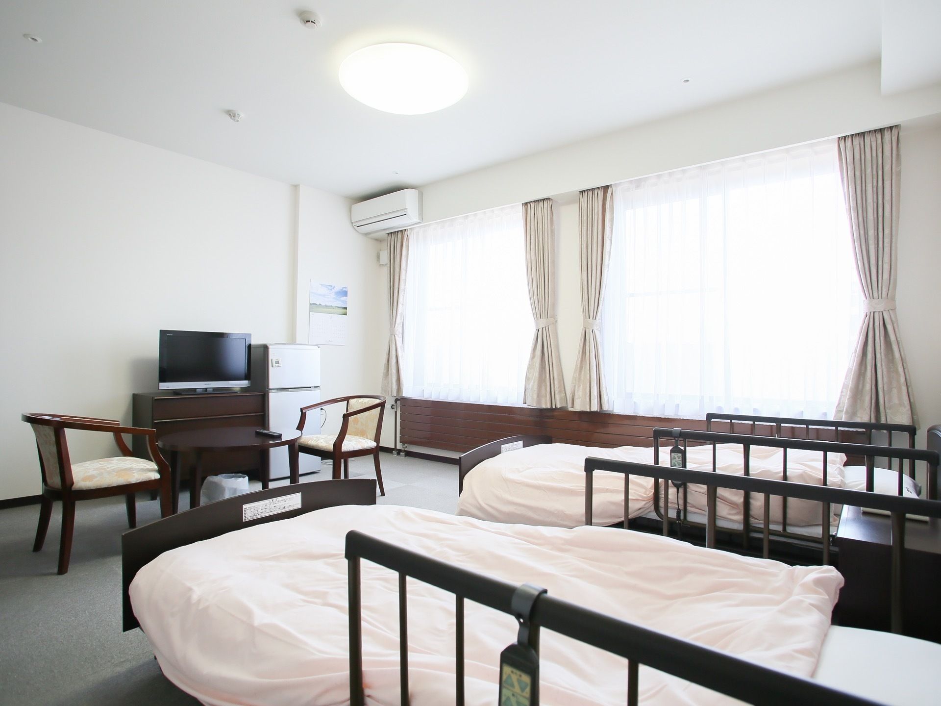 ２人部屋には、可動式のベッドが２つ置いてある。窓が並び、明るい光が差し込んでくる。テレビの前にテーブルセットもある。