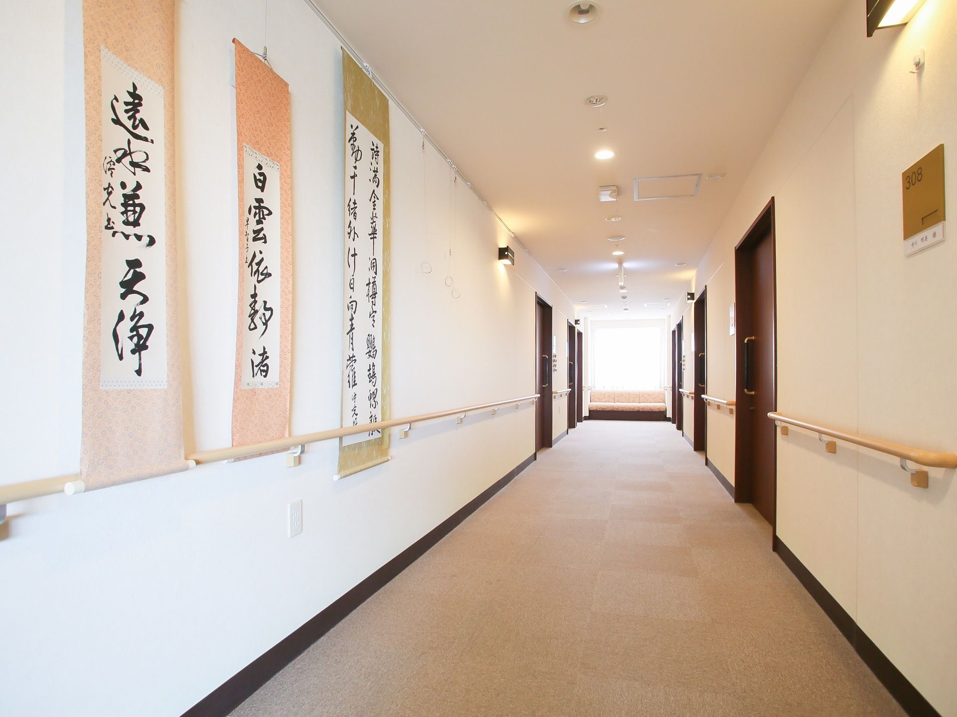 廊下の両側には、茶色のドアが並んでいる。扉のない広い壁の部分には、入居者様の書道作品などが飾ざれている。