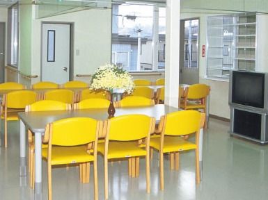 黄色いいすがセットされたダイニングテーブルが複数置かれた食堂。床に余計なものは置かれておらず、テレビ鑑賞もできる。