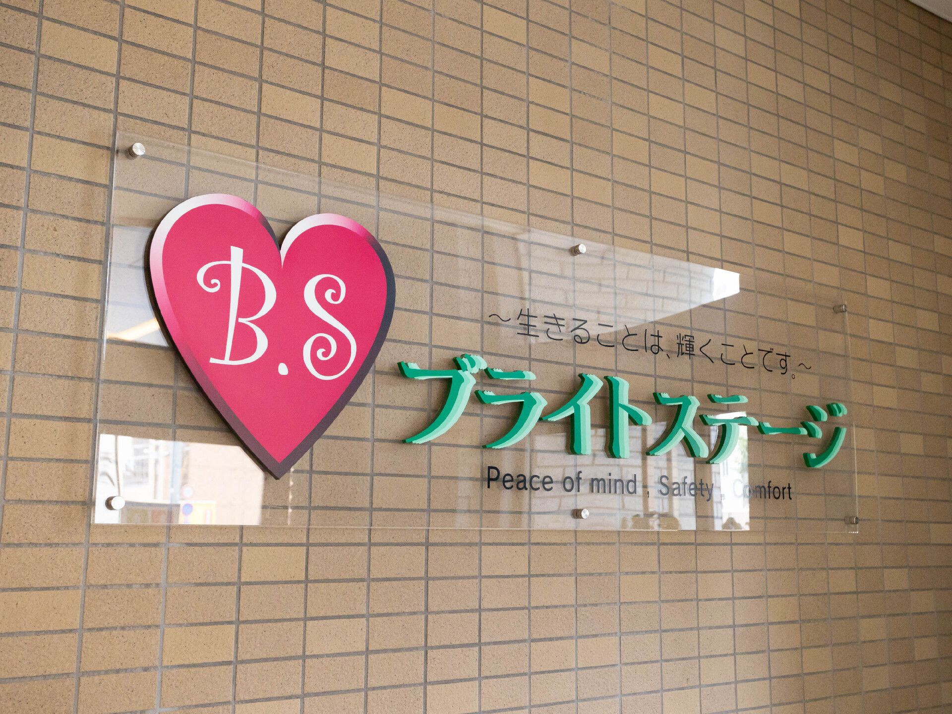 眼鏡をかけた高齢男性が福祉車両の手すりを持って車の外に出ようとしているところを若いスタッフがサポートしている。男性はスタッフに対して笑顔を向けている。