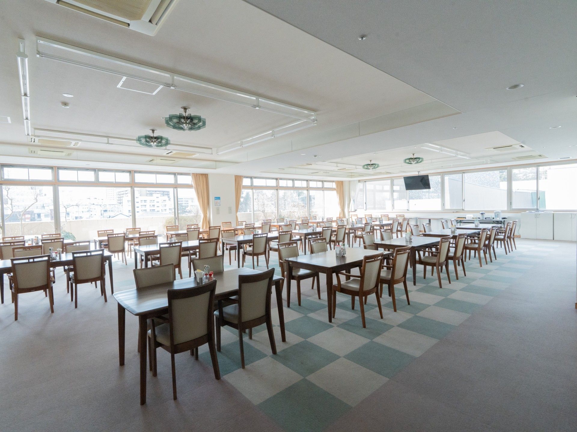 テーブルを囲んで笑顔で話しているピンクのポロシャツを着た女性スタッフと高齢女性。