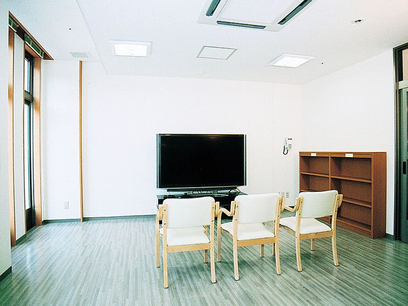 空の棚が置かれている部屋にはテレビがあり、テレビの前には白い椅子が３脚置かれている。
