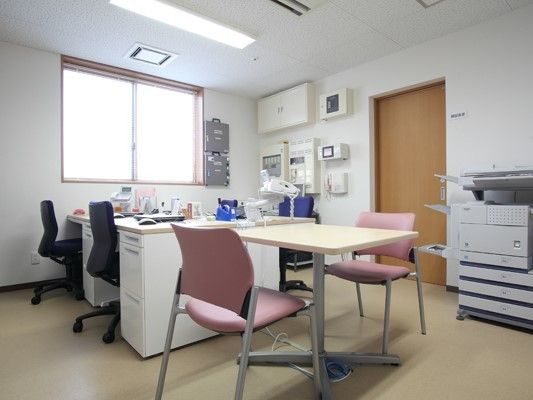 事務用デスクが並び大型のコピー機なども置かれている。手前にはテーブルセットもある。