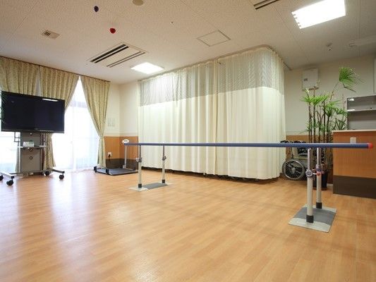 機能訓練スペースには車いすや平行棒、観葉植物に大きなテレビがある。
