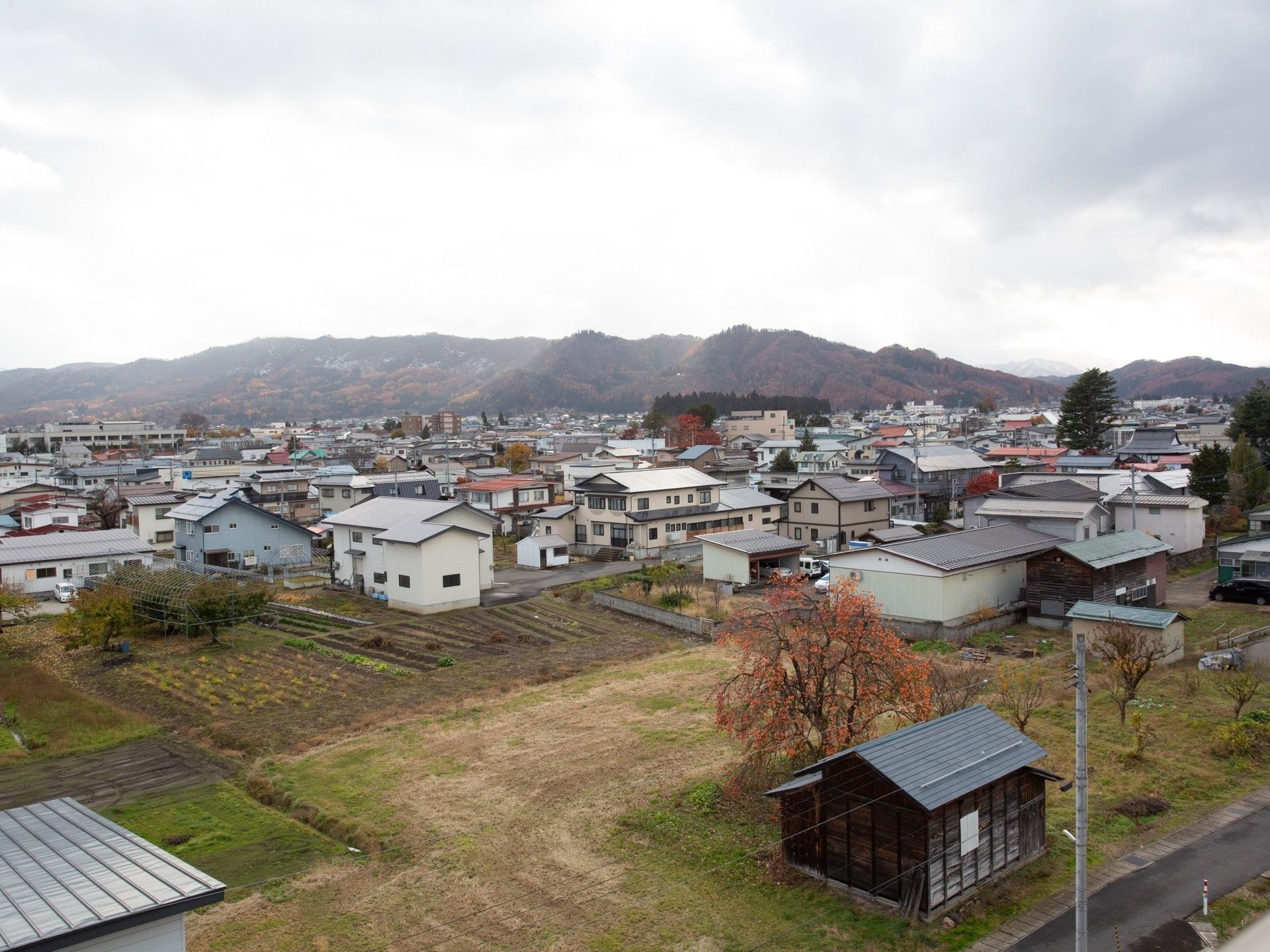 施設は市内に位置している。手前には畑や木々、そして住宅街、その向こう側にはずっと続く山並みが見える。
