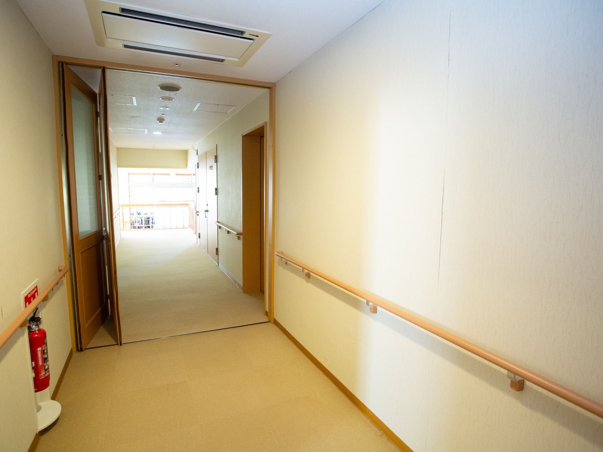 廊下には十分な横幅があり、壁には手すりがある。天井には空調設備が備わり、壁際に消火器が置かれているのが見える。