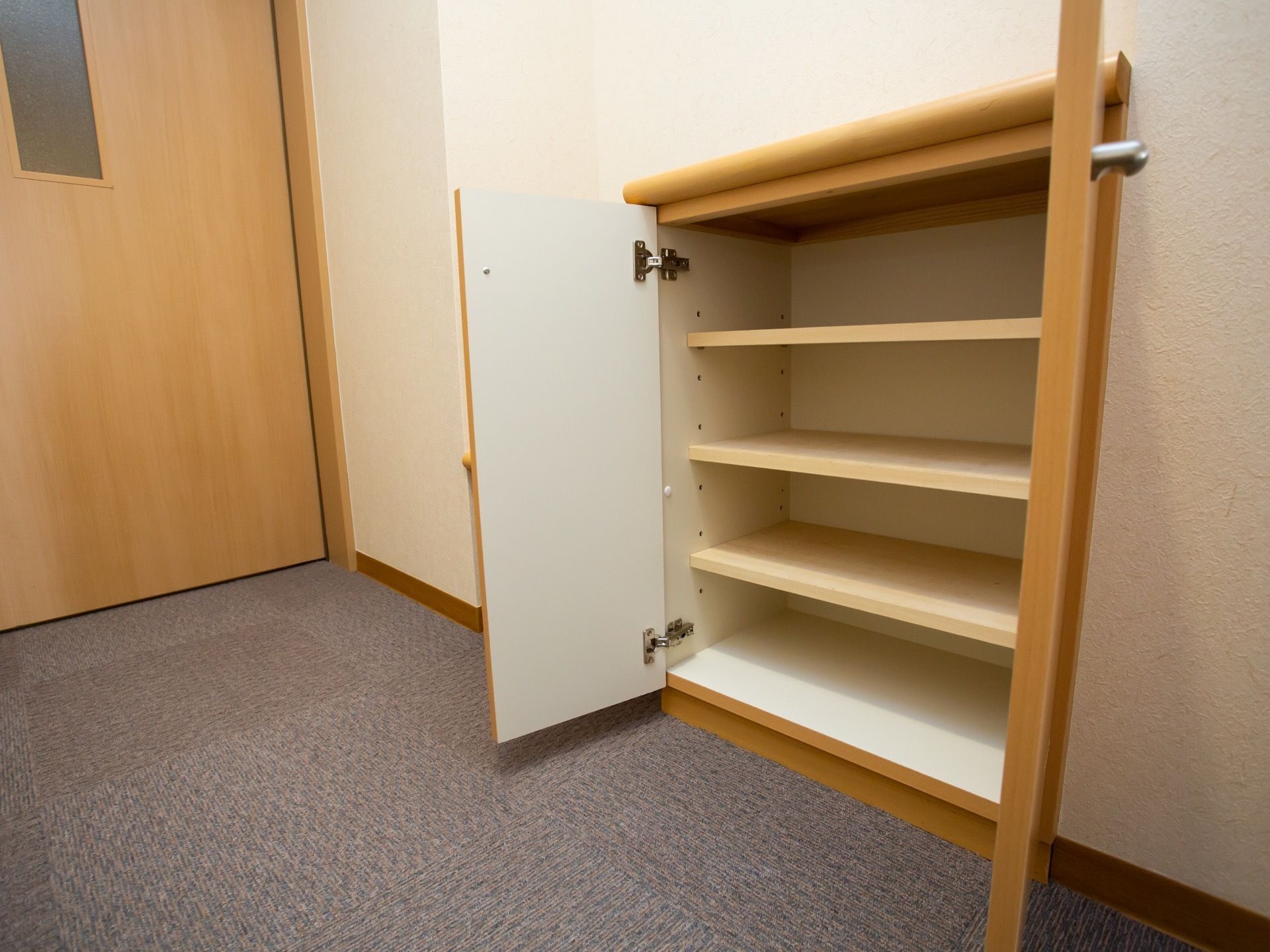 グレーのカーペット敷きの床の部屋で、ドアの近くに扉のついた靴箱が設置されている。靴箱には４段分の棚板が備わっている。