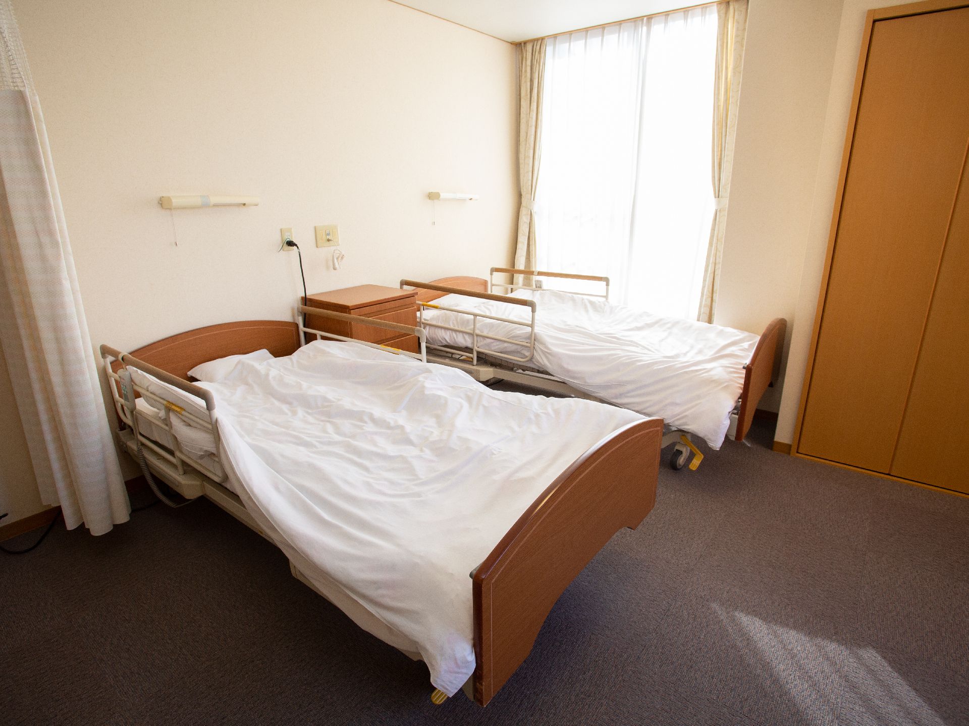 絨毯敷きの部屋にチェストを挟んで並ぶ、２つの介護用ベッド
