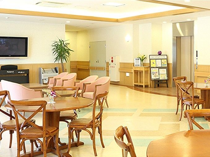 明るい広い空間に、丸テーブルと椅子のセットが置かれている。壁かけテレビがあり、その前には応接セットもある。