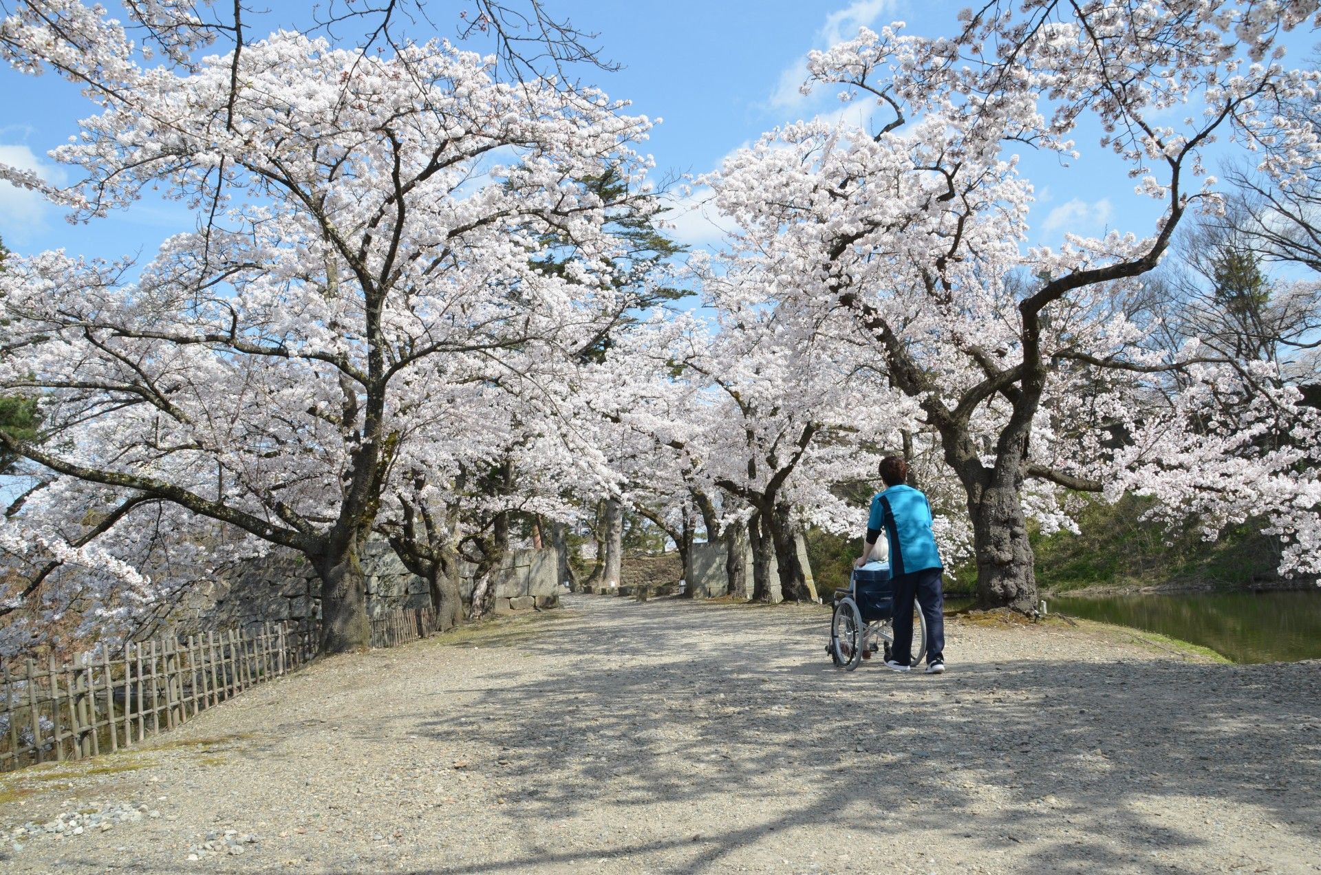 車いすに乗っている女性とその人の手を握りながらこちらを向いて笑顔を見せるスタッフ