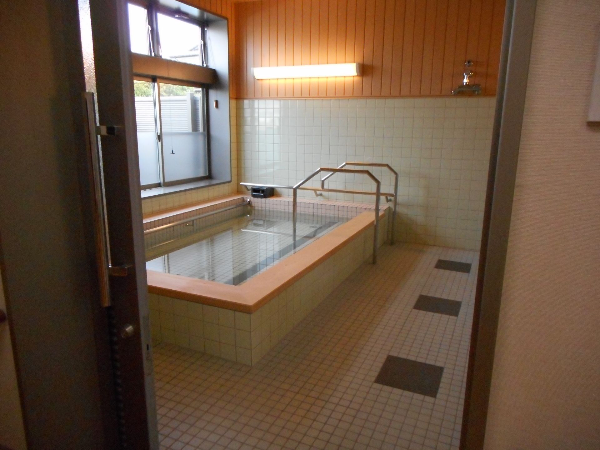 高齢者の方にタオルをかけてマッサージしているスタッフと振り返りながら会話する女性の様子