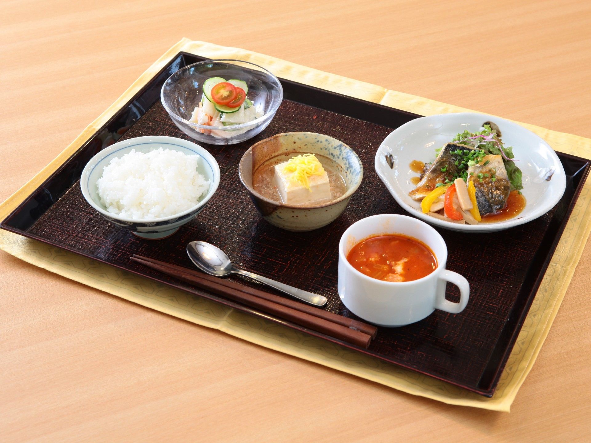 黒いトレーに並べられた食事。白いご飯にスープ、魚料理にサラダなど豪華な内容。