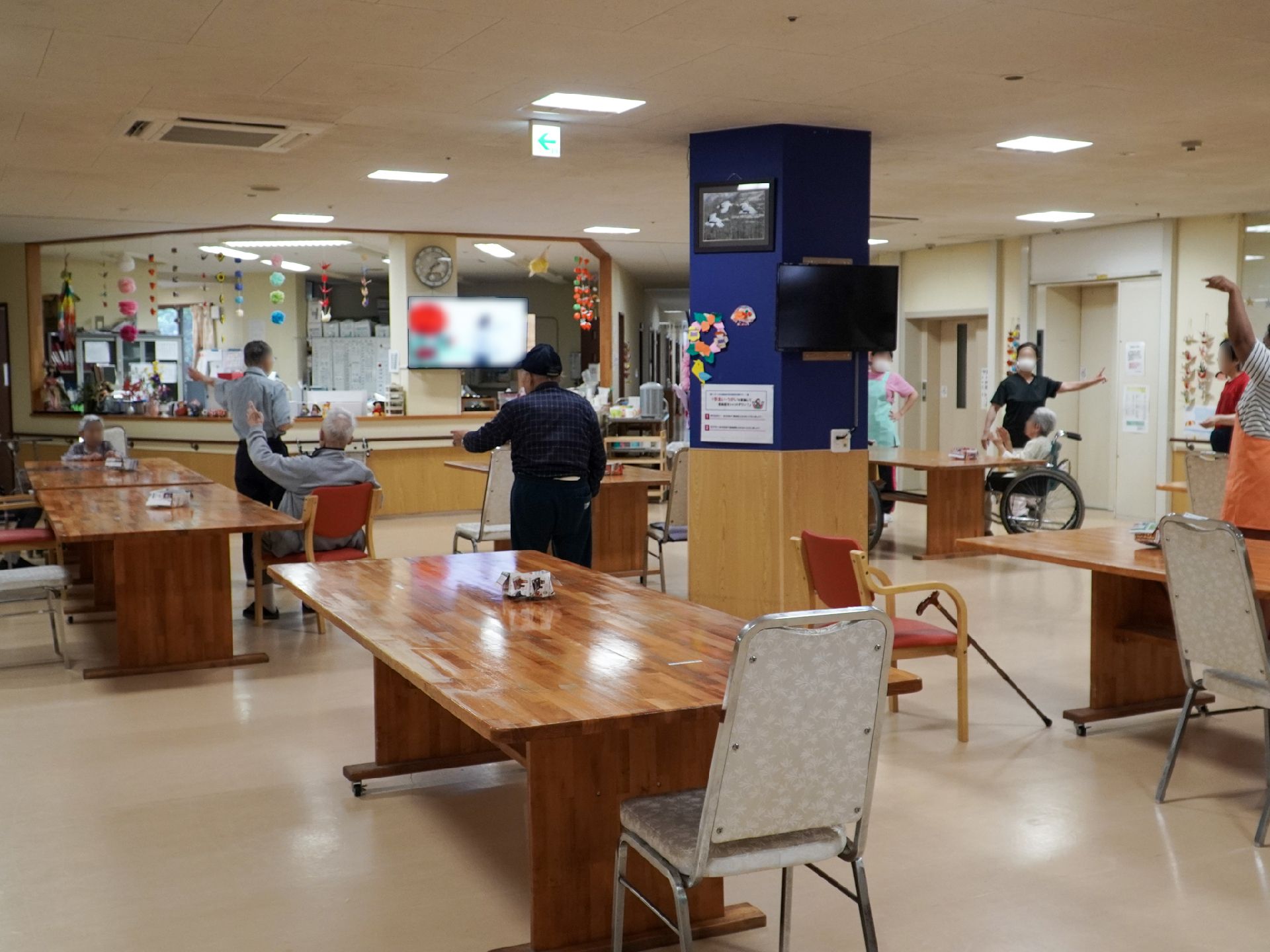 机と椅子がたくさん並んだ大きな広間で同じ動きをする入居者様