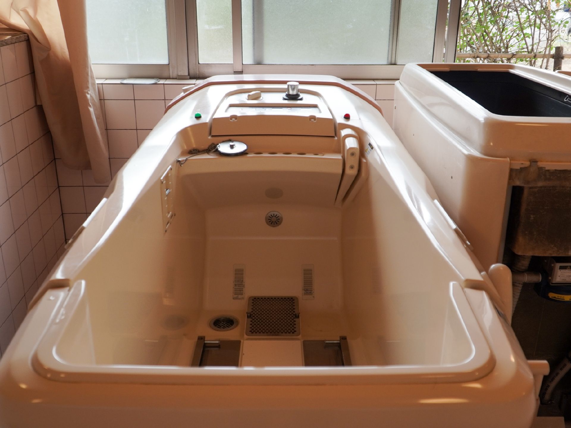 タイル調の部屋の窓際に置かれたストレッチャー浴用の機械浴槽