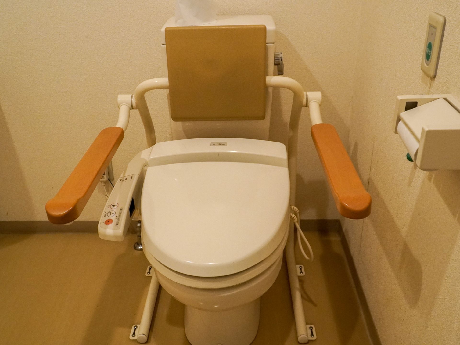 部屋の一角に置かれた手すりが付いているトイレ