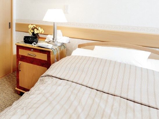 寝具付きのベッドが置かれている部屋にはランプや花が生けられた花瓶が置かれた床頭台がある。