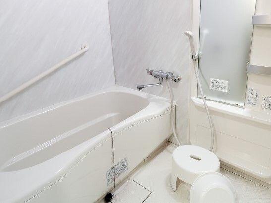 手すりが設置された一人用の浴槽がある浴室には鏡やシャワーもあり、白でまとめられている。