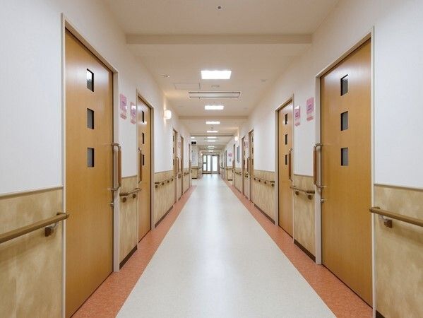 まっすぐな廊下の両サイドに手すりが付き、居室のドアはスライド式。フロアの中央と両サイドの色が異なる。