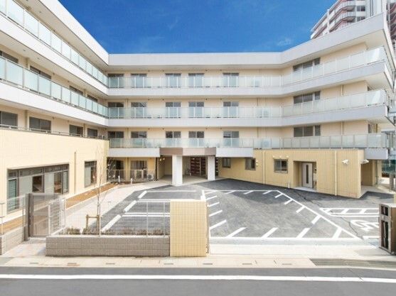 4階建ての建物はベージュ系の外壁で、コの字のような形。中央には広い駐車場が付いている。
