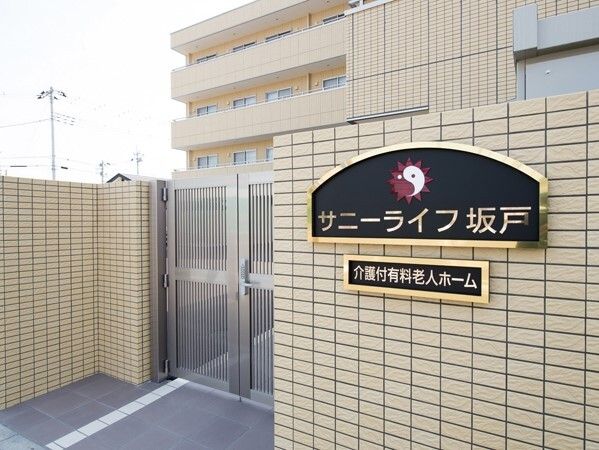 ベージュの重厚感のある建物が後ろにあり、手前には施錠ができる門があり、ホーム名が書かれたプレートが貼られている。