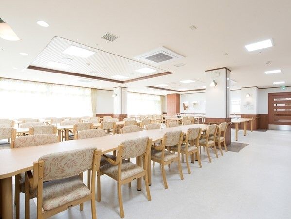 広々とした食堂は明るい雰囲気。ベージュの椅子がセットされた木製のテーブルセットが多く置かれている。