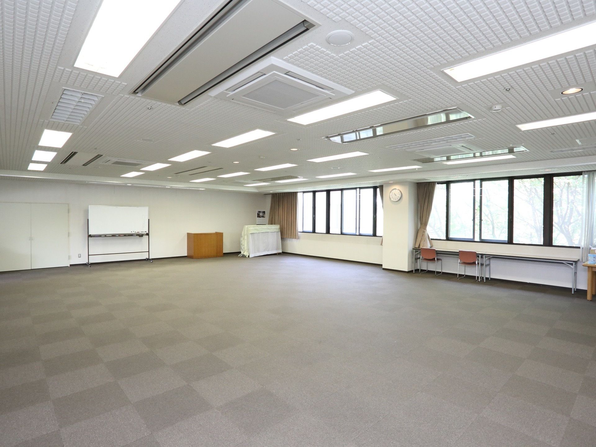 とても広い空間になっており、壁際にはホワイトボードなどが置かれている。腰高の窓があり、ベージュのカーテンが掛けられている。