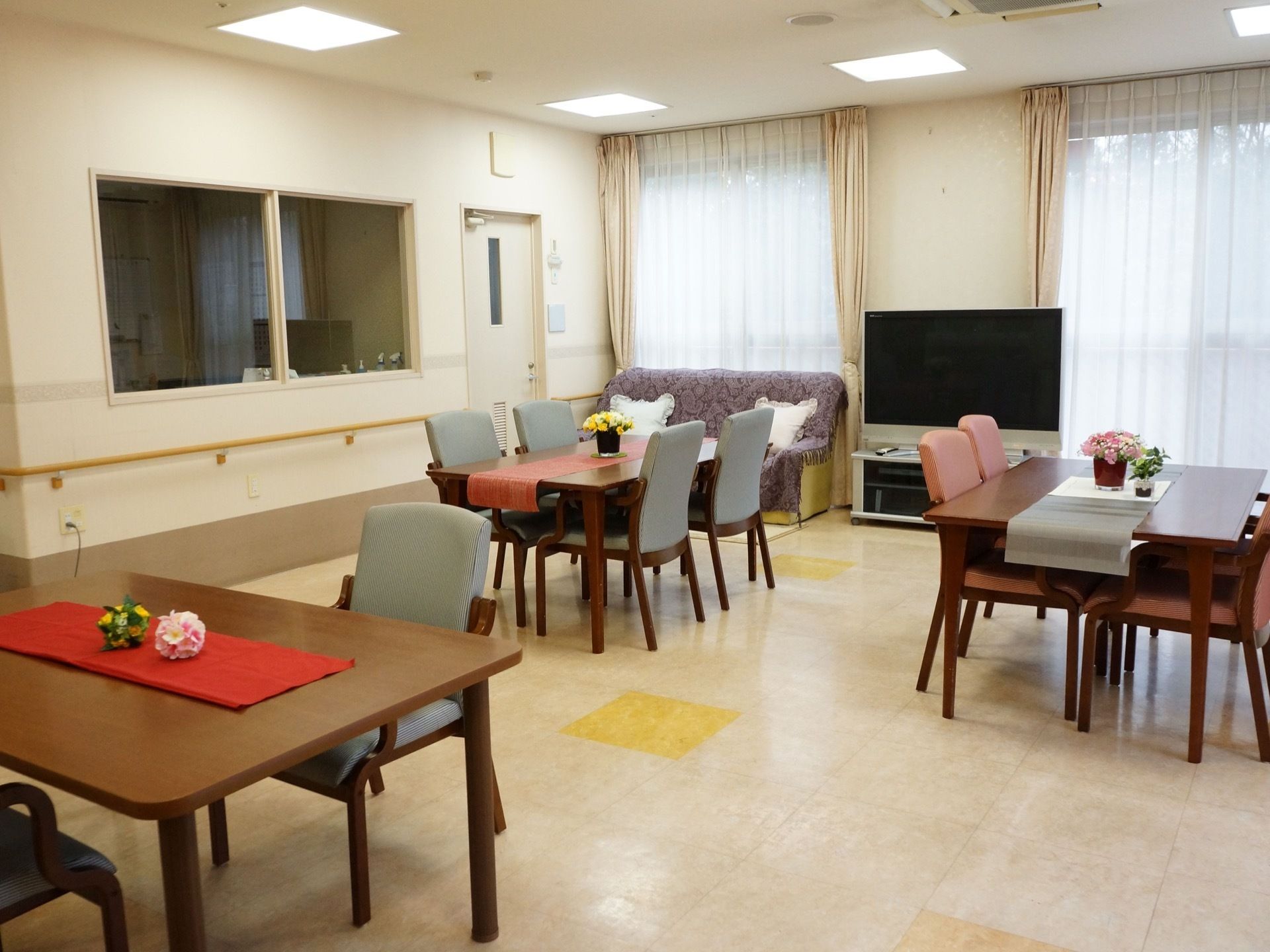 リビングルームの奥には大きな窓が左右にあり、その真ん中にテレビが置いてある。天井には、四角い照明器具が付いている。