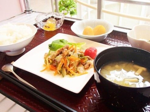 野菜炒めをメインとして、白いご飯に味噌汁、野菜の和え物やフルーツなどがそれぞれ器に盛られている。