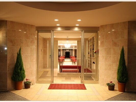 赤いマットが敷かれたエントランス周辺には緑が置かれ、赤いマットが敷かれている。風除室の向こうには共有スペースが広がっている。