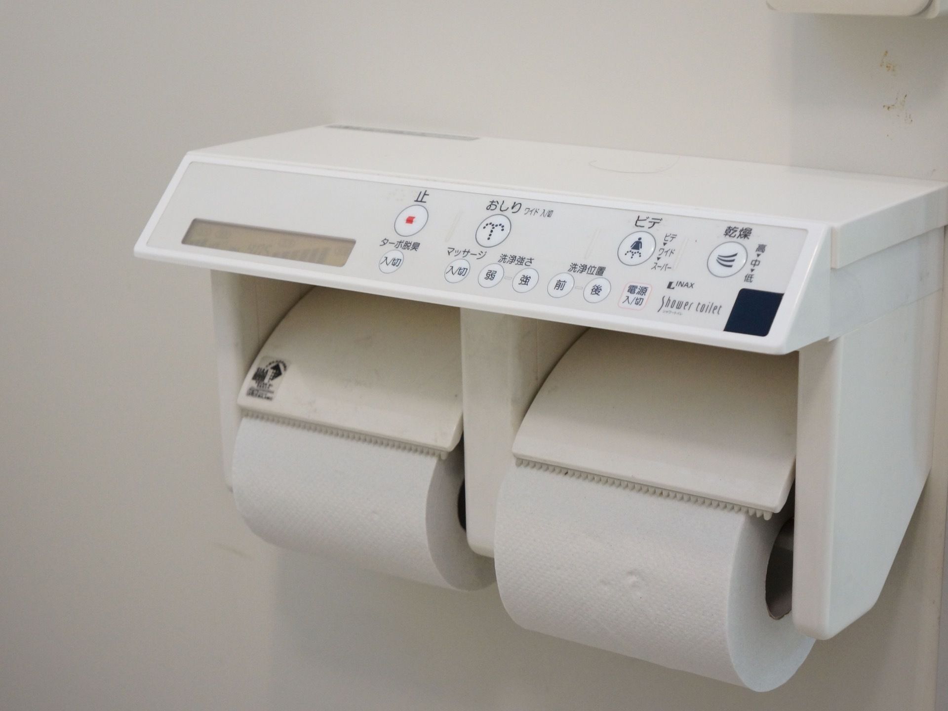 トイレットペーパーが２つ取り付けられる白を基調としたホルダーで、コントロールパネルが設置されている。