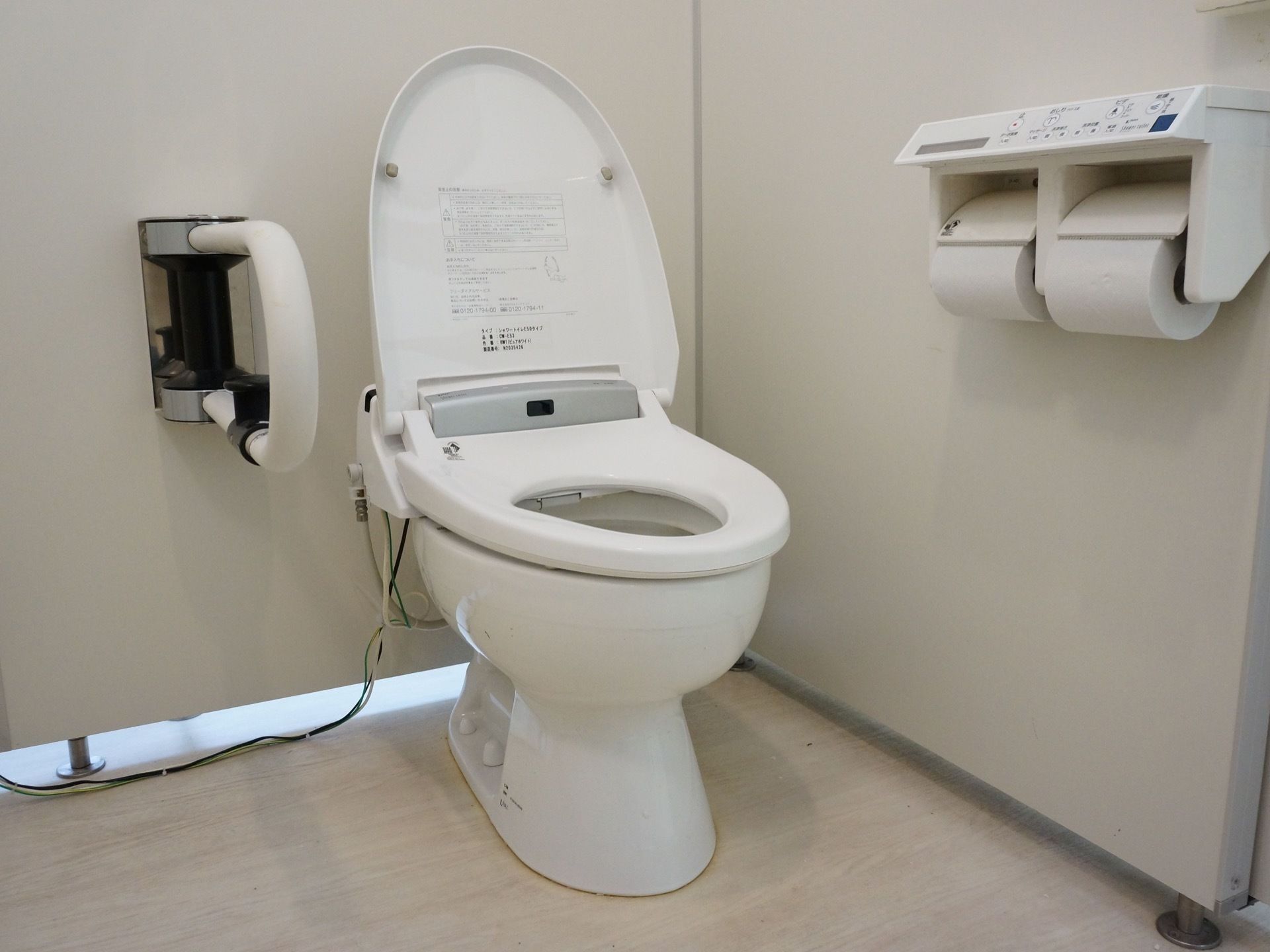 温水洗浄機能付きのシンプルで、掃除の行き届いたトイレである。立ち座りの際に掴まれる、手すりが設置されている。