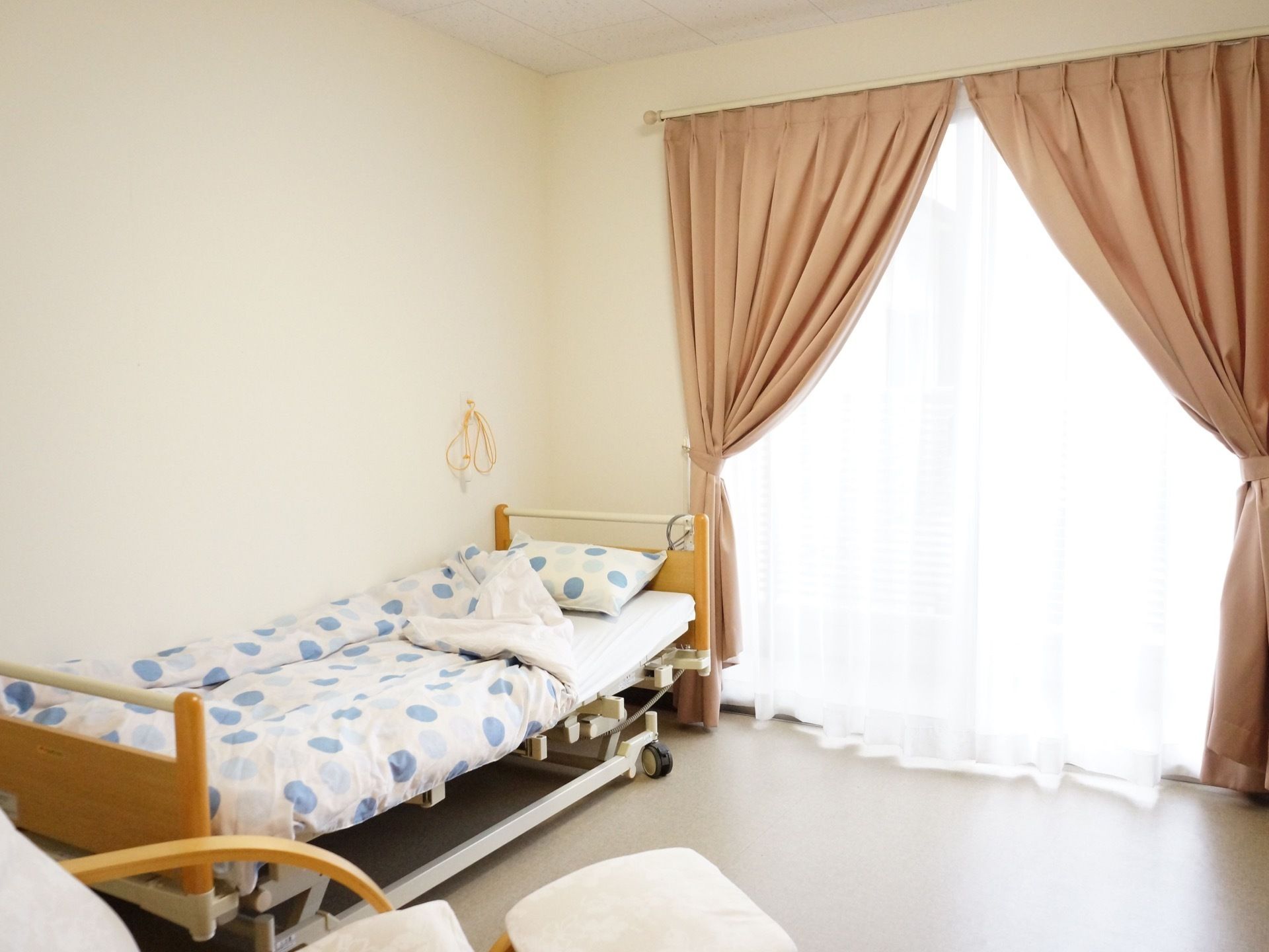 白を基調とした個室には、大きな窓があり、たっぷりと太陽の光が入る。室内には、介護ベッドや椅子が置かれている。