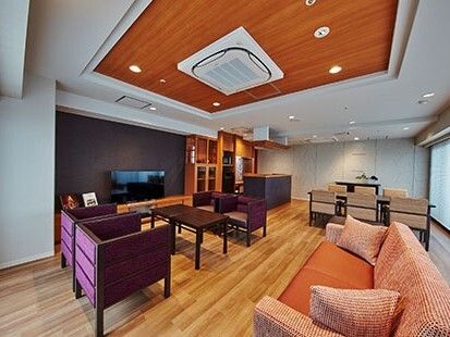 オレンジ色のソファやダイニングテーブルセットが置かれ、テレビやキッチンも設置されている。
