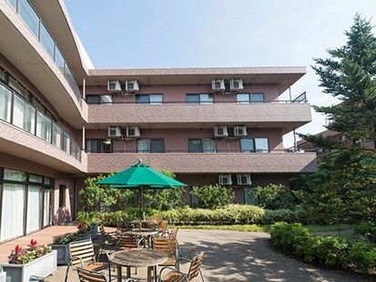 レンガ調のブラウンの外壁。3階建てで中庭にはパラソル付きのテーブルセットが置かれ、花も植えられている。